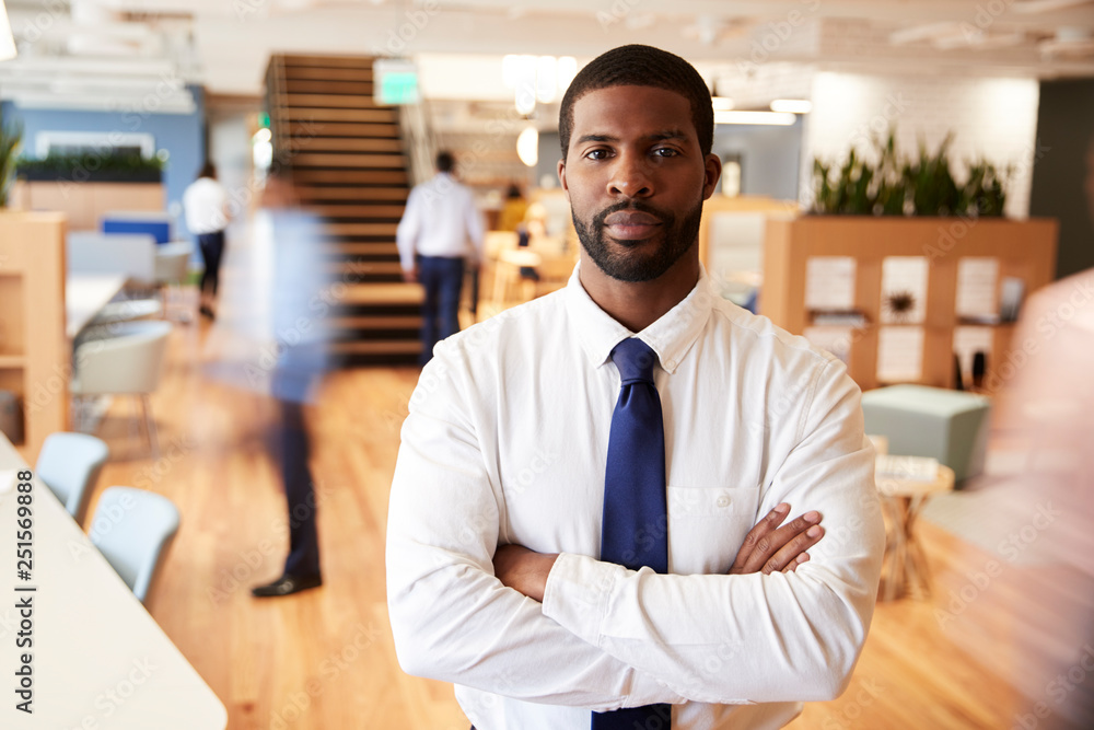 Fototapeta premium Portrait Of Businessman In Busy Modern Office With Blurred Colleagues Working In Background