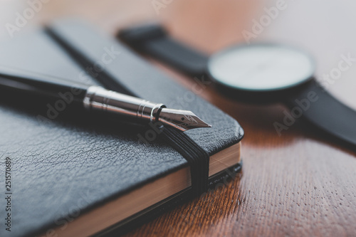A fountain pen on a notebook near a watch photo
