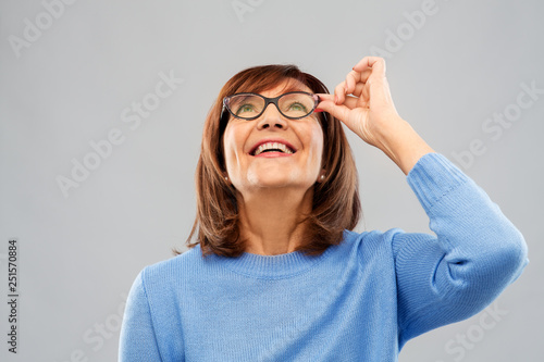 vision and old people concept - portrait of smiling senior woman in glasses looking up over grey background