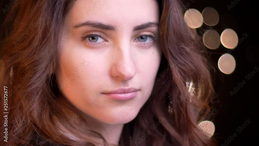 Close-up portrait in profile of young caucasian girl watching seriously and flirtingly into camera on blurred lights background. Close-up portrait in profile of young caucasian girl watching seriously and flirtingly into camera on blurred lights background.