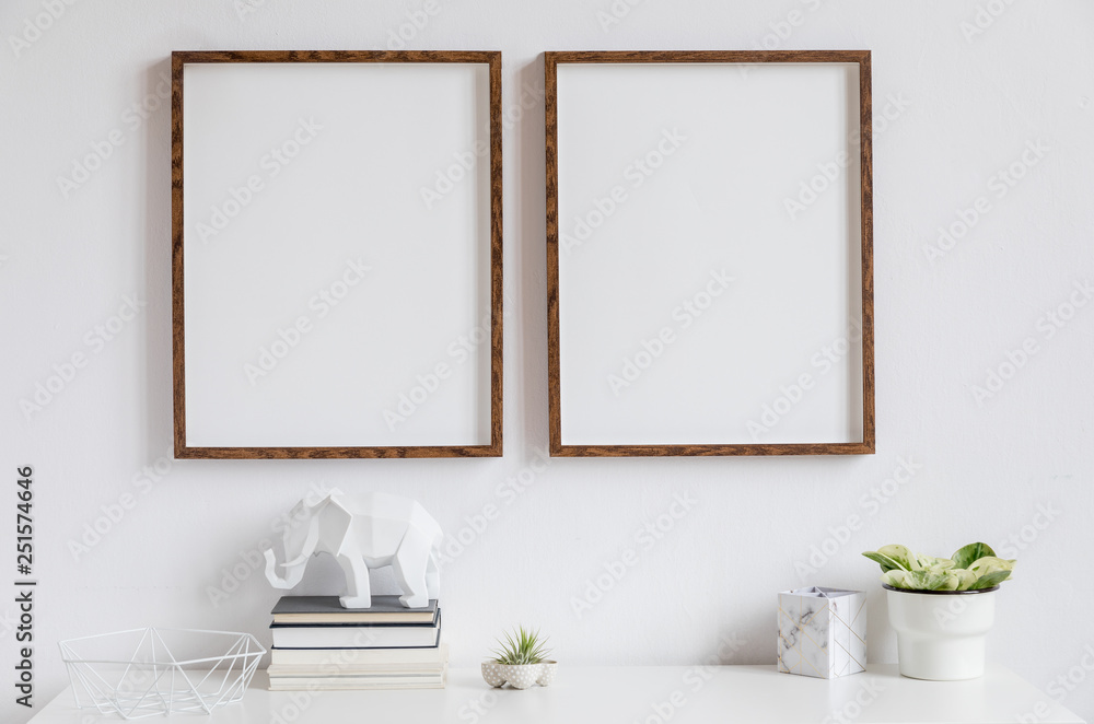Fototapeta Stylowy biały wystrój wnętrza z dwiema brązowymi drewnianymi ramkami na zdjęcia na białej półce z książkami, piękną rośliną w stylowej doniczce, figurką słonia i akcesoriami do domu.