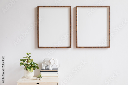 Stylish home interior with two brown wooden mock up photo frames above the wooden shelf with books, plants, and elephant figure. Modern concept of white room decor. 