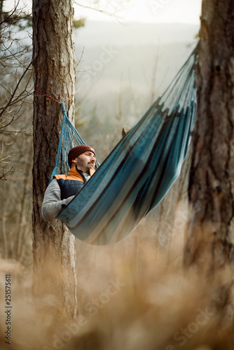 Young happy man relaxing lying in hammock on top of mountain.