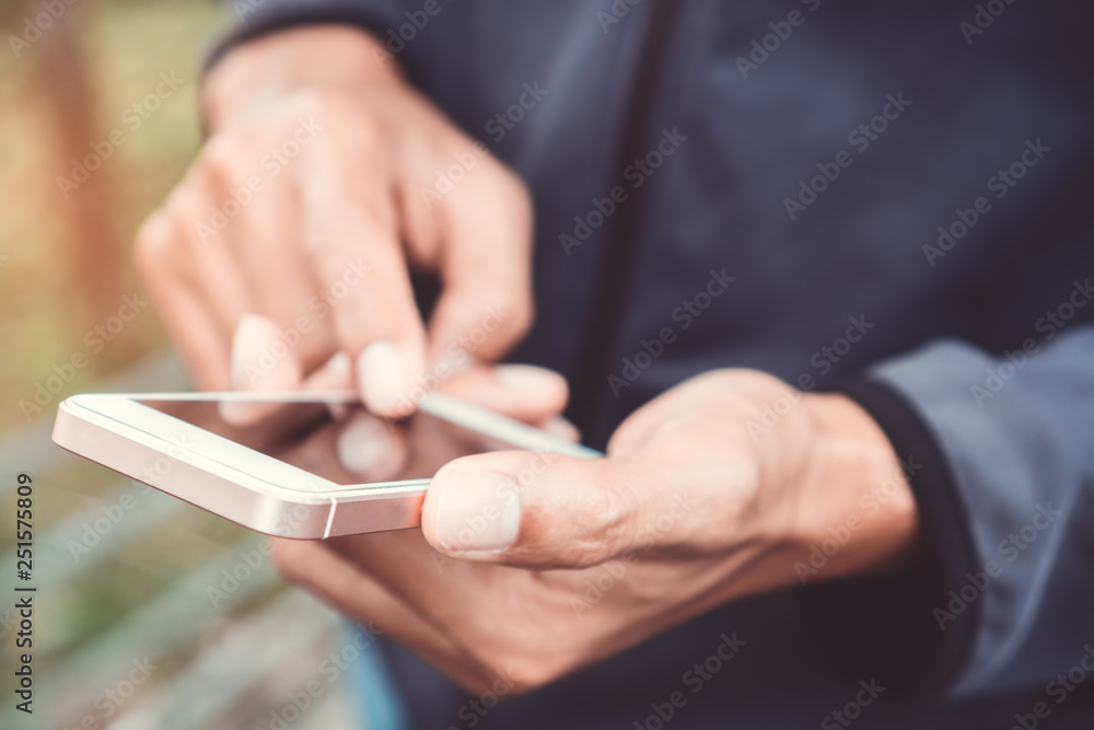 Close up man hand hold using smart phone on outdoor park street background.