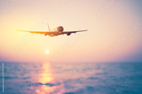 Airplane flying over blur tropical beach with smooth wave and sunset sky abstract background.