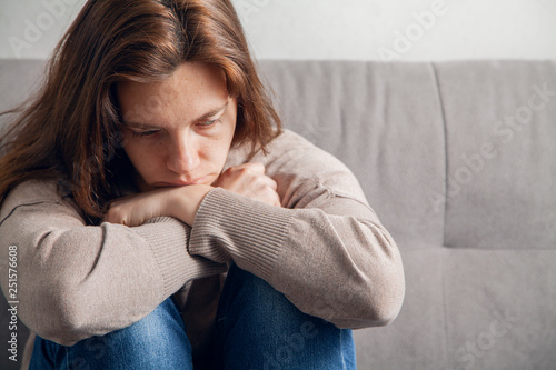  A lonely young woman sits with her arms folded to her feet and sad.