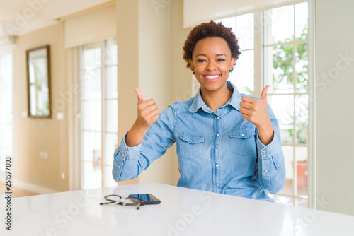 Young beautiful african american woman success sign doing positive gesture with hand, thumbs up smiling and happy. Looking at the camera with cheerful expression, winner gesture.