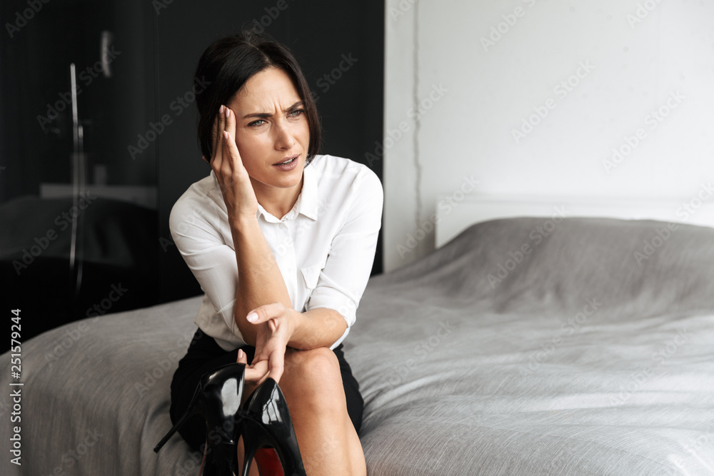 Obraz premium Beautiful tired business woman with headache in bedroom indoors at home sitting on bed.