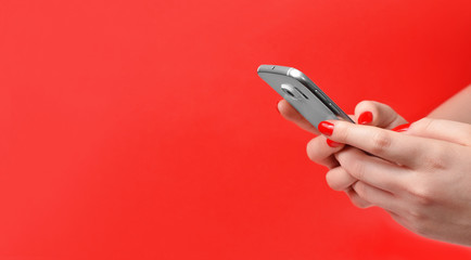 Female hands holding the smartphone isolated on red background with free space