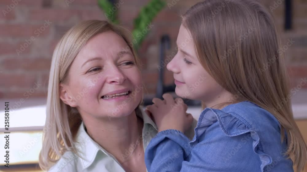 happy motherhood, little smiling child girl tells beloved mum whispering secrets in ear close up at home happy motherhood, little smiling child girl tells beloved mum whispering secrets in ear close up at home