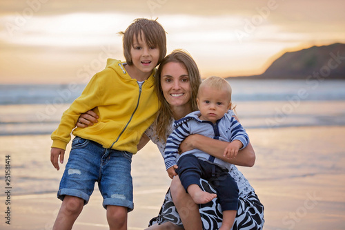 Young mother with her beautiful children, enjoying the sunset over the ocean on a low tide in Devon