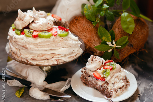 ropical aquafaba cake with kiwi, strawberry and coconut cream on dark table with ingredients and flowers photo