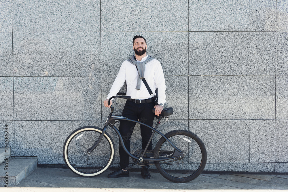 Fototapeta premium Businessman standing against building wall with his bicycle.