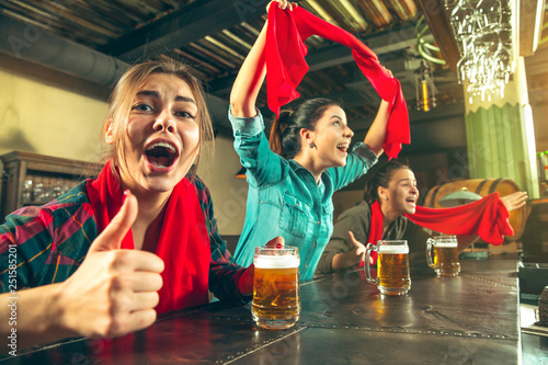 Sport, people, leisure, friendship, entertainment concept - happy female football fans or good young friends drinking beer, celebrating victory at bar or pub. Human positive emotions concept