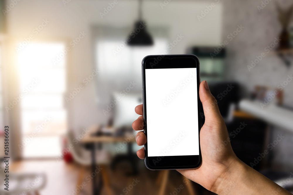 Hand holding white mobile phone with blank white screen in office. Hand holding white mobile phone with blank white screen in office.