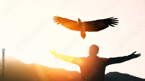 Obraz na płótnie Man raise hand up on top of mountain and sunset sky with eagle bird fly abstract background