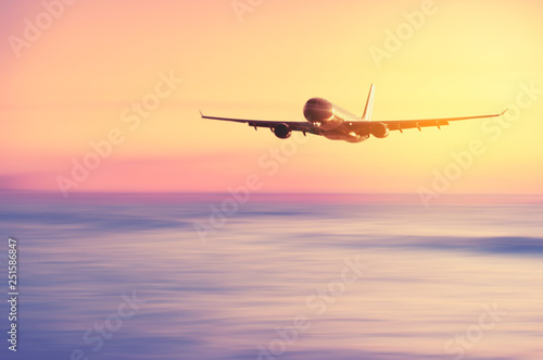 Airplane flying over blur tropical beach with smooth wave and sunset sky abstract background.