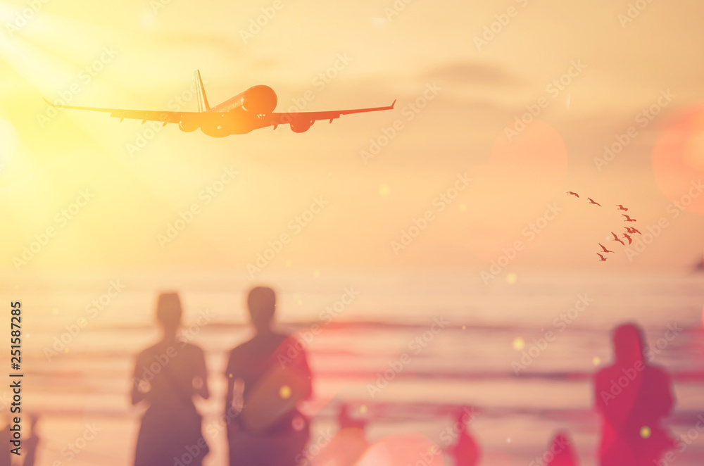 Fototapeta premium Airplane flying over blur people relax on tropical sunset beach with bokeh sun light and birds abstract background.