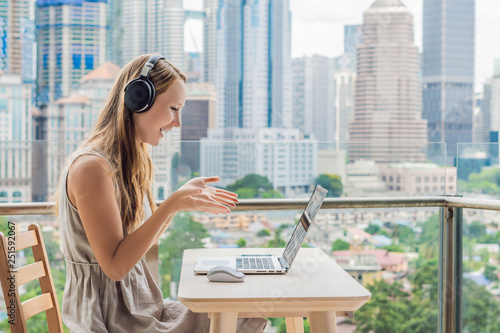 Young woman teaches a foreign language or learns a foreign language on the Internet on her balcony against the backdrop of a big city. Online language school lifestyle photo