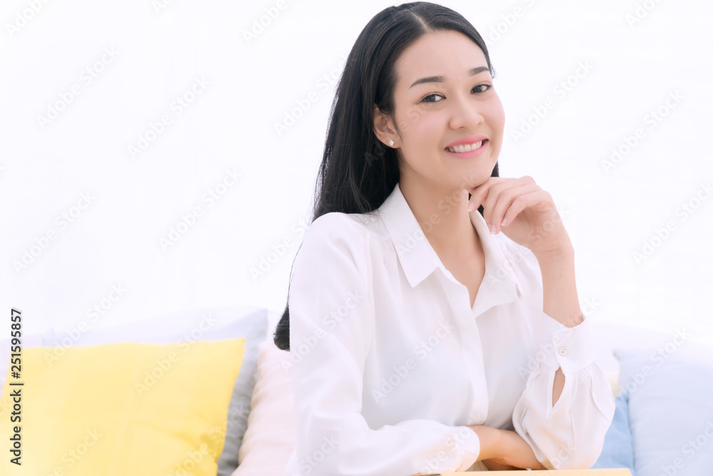 Lifestyle relaxation concept. Cheerful smiling young woman sitting on white couch with pillow and yellow book in living room at home Lifestyle relaxation concept. Cheerful smiling young woman sitting on white couch with pillow and yellow book in living room at home