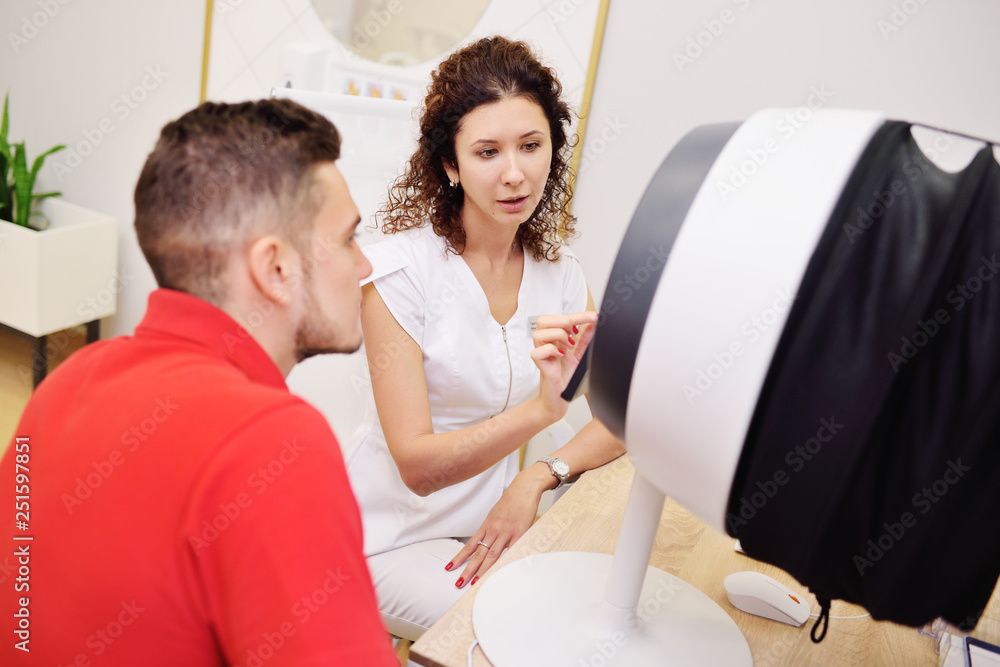Fototapeta premium facial skin diagnostics equipment for dermatology and cosmetology. A cosmetologist analyzes the skin condition of a young handsome male patient.