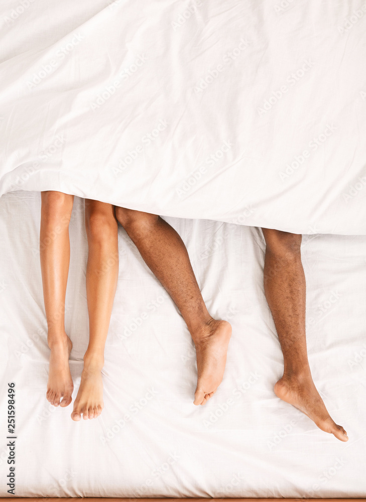 Male and female legs under duvet lying on bed - obrazy, fototapety, plakaty 
