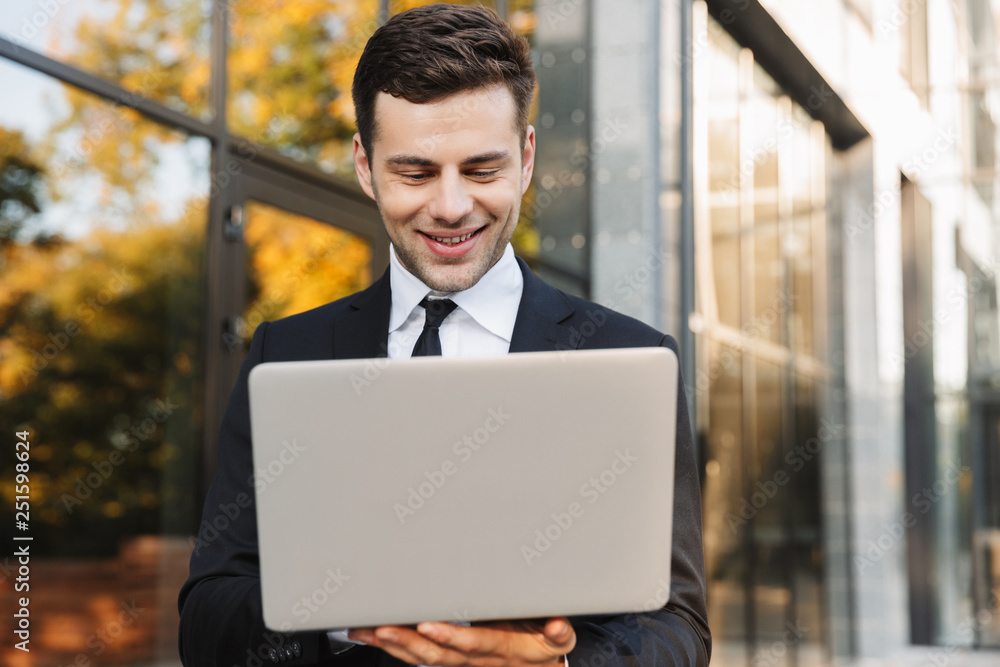 Young businessman walking outdoors using laptop computer. Young businessman walking outdoors using laptop computer.