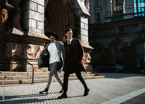 Two fashion beautiful man models posing on city street. Wearing in classic and casual closes. Suit, coat, shirt, sweater, boots. Man model street test.