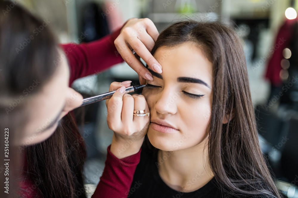 Process of making makeup. Make-up artist working with brush on model face. Portrait of young woman in beauty saloon interior. Applying tone to skin.