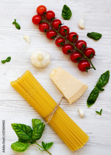 Spaghetti, tomatoes, basil, parmesan, garlic. Ingredients for cooking pasta on a white wooden background, flat lay. From above.