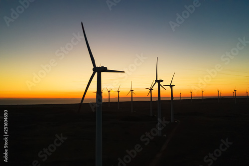 The movement of wind turbines blades in the field against the backdrop of a bright orange sunset wind park. Silhouettes of windmills with a bird's-eye view. Alternative energy sources. Drone, slide up