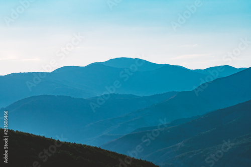 Landscape of mountains against the blue sky and clouds. Forest of pine trees. The tops of the mountains in the winter in a small haze. Panorama of the peaks of the beautiful tree-covered mountains