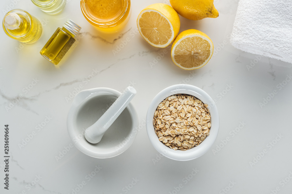 top view of bowl with oat flakes, pounder, lemons and various components for homemade cosmetics on white surface top view of bowl with oat flakes, pounder, lemons and various components for homemade cosmetics on white surface