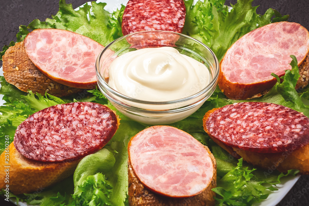 Several sandwiches with sausage and salami and sauce on a plate, close up Several sandwiches with sausage and salami and sauce on a plate, close up