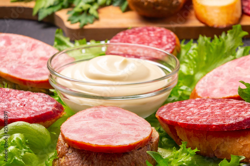 Several sandwiches with sausage and salami and sauce on a plate, close up