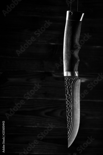 Old hunting knife hanging on the background of carved boards in the dark
