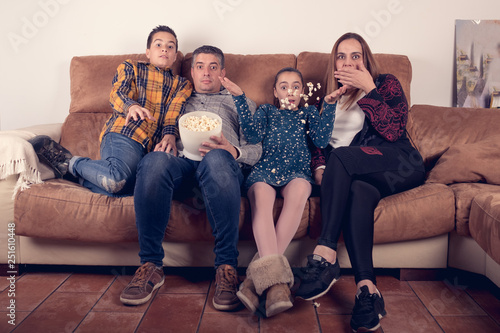 family watching horror movie on the couch at home and eating popcorn