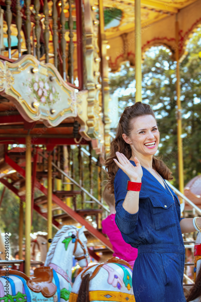 smiling elegant tourist woman riding on carousel and waving