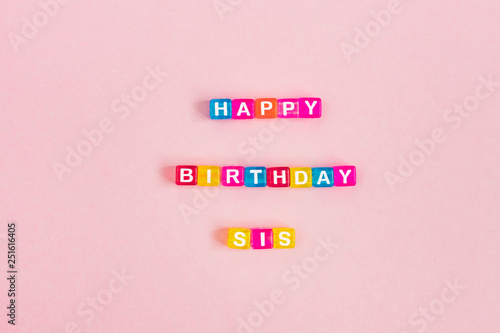 Happy birthday sis inscription made of colorful cube beads with letters. Festive pink background concept with copy space