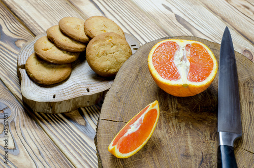 Sicilian oranges and knife with black knob rests on a wooden board, which stands on a wood table