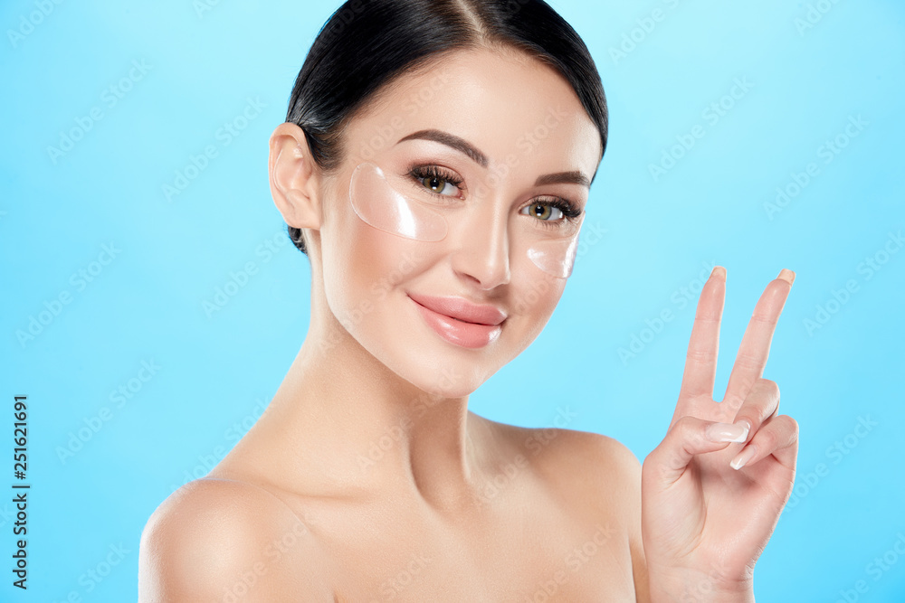 Beautiful girl with nude make up and naked shoulders at studio background, invisible eye patches on face, close up portrait, blue background. Beautiful girl with nude make up and naked shoulders at studio background, invisible eye patches on face, close up portrait, blue background.