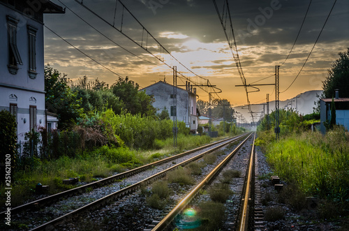 Railway tracks with old buildings on sides, wires above and Tuscany hills and mountains with dramatic cloudy sky background, evening, dusk, twilight view, near Lucca town, Italy photo