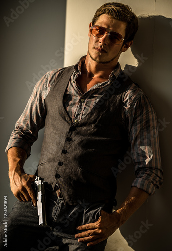 Young Caucasian male holding a gun in a sunset hotel