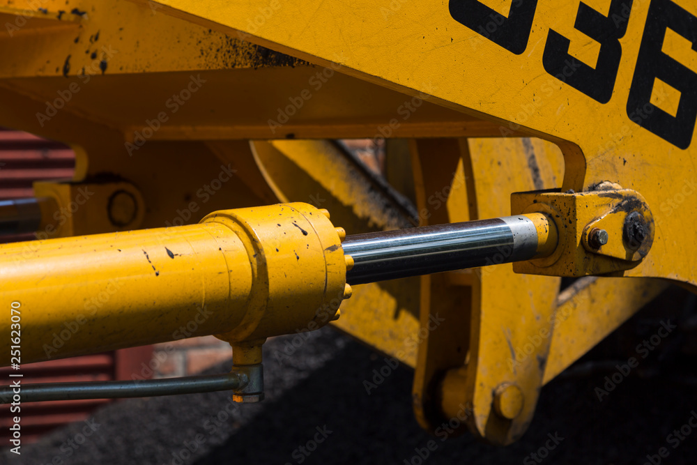 Shiny hydraulic cylinder rod of yellow road machinery close-up Shiny hydraulic cylinder rod of yellow road machinery close-up