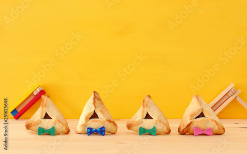 Purim celebration concept (jewish carnival holiday). Traditional hamantaschen cookies with funny bow over wooden table and yellow background.