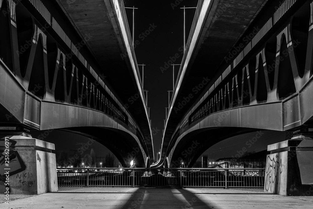 Under a large bridge at night, a massive bridge construction at night, minna todenhagen bridge at night, black and white photo