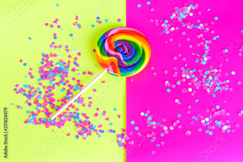 Colorful rainbow lollipop swirl  on wooden stick and and confetti on happy bright color surge background. Summer Vacation, invitation card on party, travel concept.Copy space.Top view.