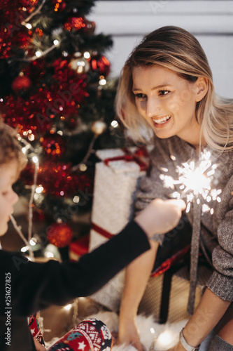 Smiling mother and son hold sparklers at home during Christmas