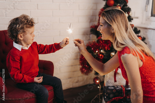 Smiling mother and son hold sparklers at home during Christmas