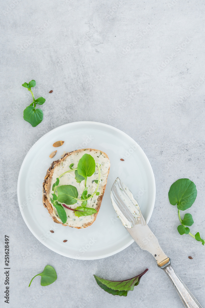 Frisches Brot, mit veganem Frischkäse und Salat auf einem hellen Betonhintergrund